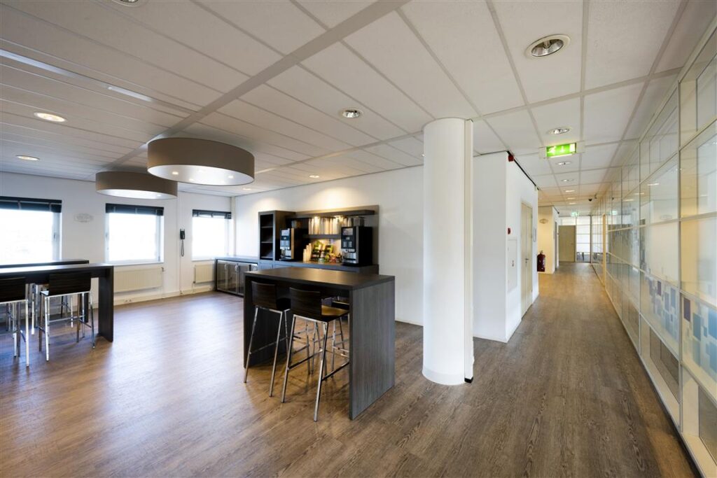 Moderne kantoorpauzeruimte aan de Paasheuvelweg met hoge tafels, barkrukken en een koffieautomaat.