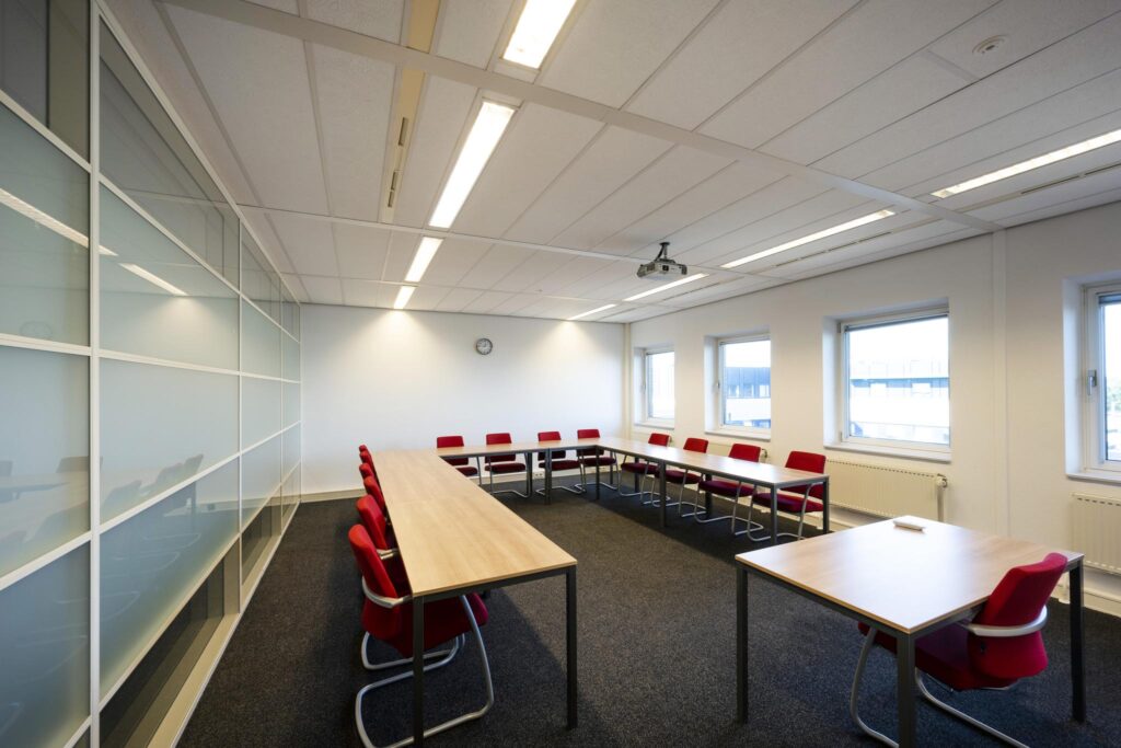 Vergaderruimte aan de Paasheuvelweg met U-opstelling van tafels, rode stoelen en plafondbeamer.