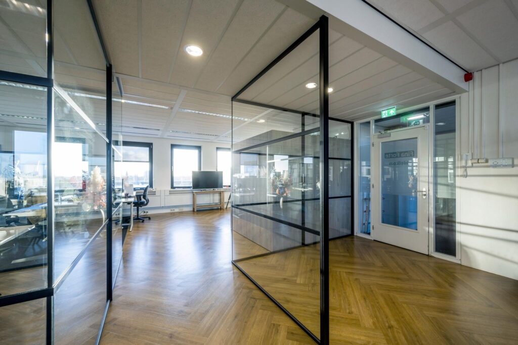 Modern kantoorinterieur aan de Radarweg met glazen wanden, houten visgraatvloer en veel natuurlijk licht.