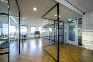 Modern kantoorinterieur aan de Radarweg met glazen wanden, houten visgraatvloer en veel natuurlijk licht.