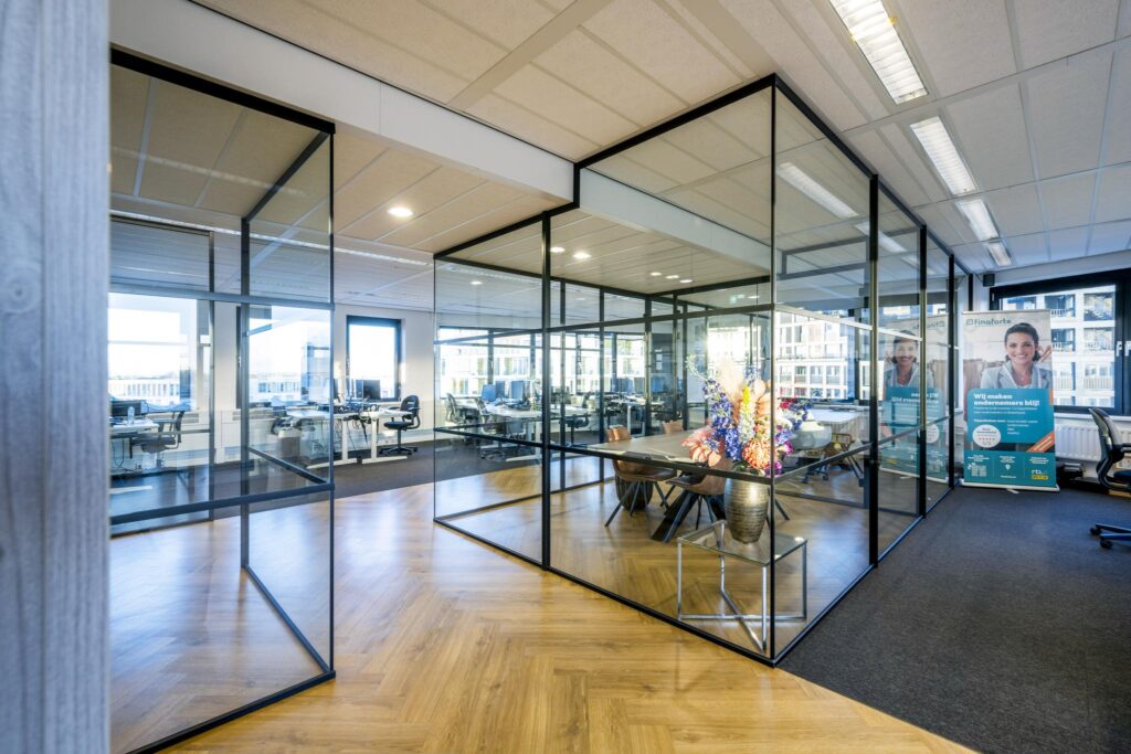 Modern kantoorinterieur aan de Radarweg met glazen vergaderruimtes, werkplekken en kleurrijk bloemstuk.