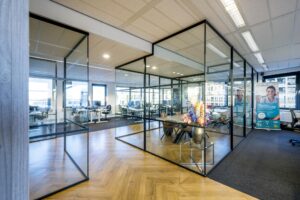 Modern kantoorinterieur aan de Radarweg met glazen vergaderruimtes, werkplekken en kleurrijk bloemstuk.