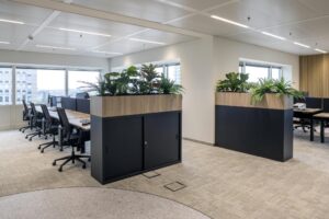Modern open-plan office at Amstelplein with workstations, indoor plants, and large windows.