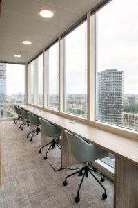Modern workspace with desk chairs along large windows overlooking Amstelplein and a high-rise skyline.