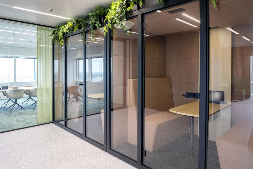 Modern office space at Amstelplein with glass-walled meeting rooms, indoor plants, and contemporary furniture.