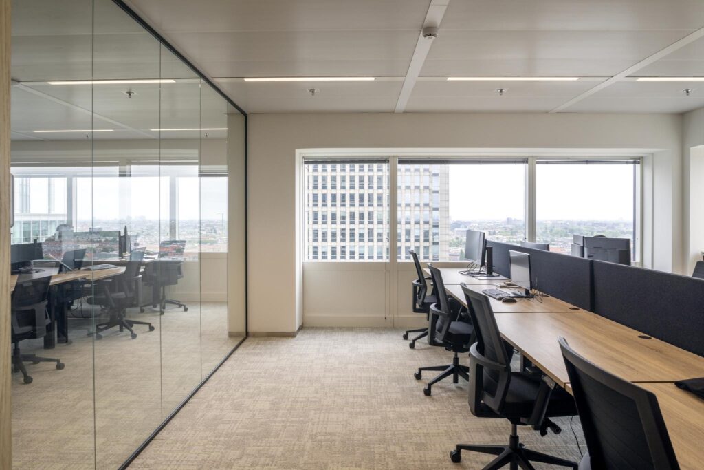 Modern open-plan office space at Amstelplein with workstations and city view through large windows.