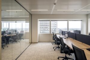 Modern open-plan office space at Amstelplein with workstations and city view through large windows.