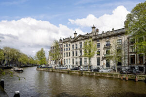 Monumentale panden aan de Herengracht in Amsterdam met uitzicht op de gracht en een passerende rondvaartboot.