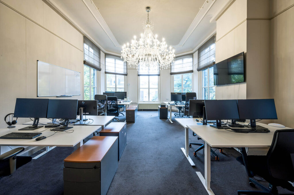 Modern kantoor aan de Herengracht met open werkplekken, grote ramen en een opvallende kroonluchter.