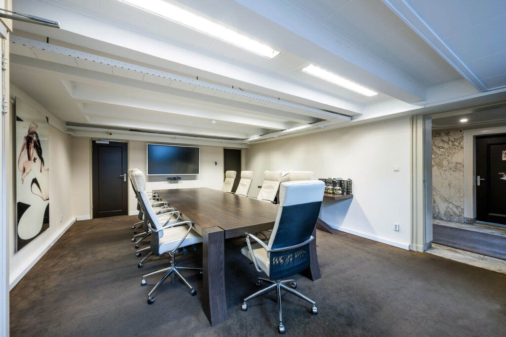 Vergaderruimte aan de Herengracht met een lange houten tafel, luxe bureaustoelen en een groot presentatiescherm aan de muur.