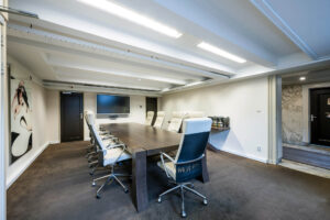 Vergaderruimte aan de Herengracht met een lange houten tafel, luxe bureaustoelen en een groot presentatiescherm aan de muur.