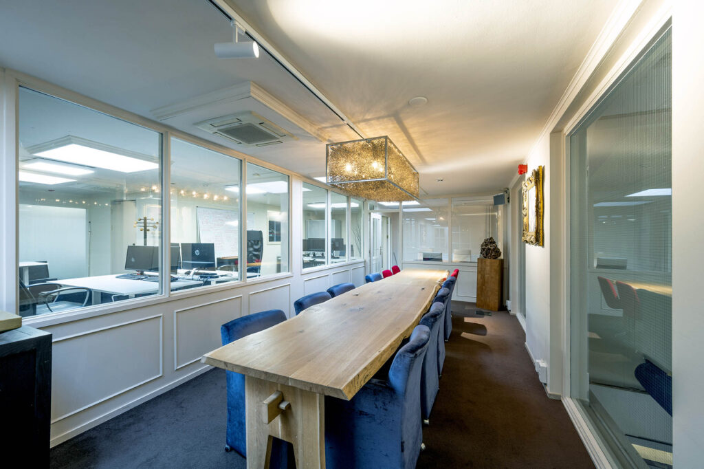 Vergaderruimte met een lange houten tafel, omringd door blauwe en rode stoelen, in een modern kantoor aan de Herengracht.