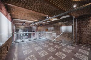 Uitkijkpunt op een tussenverdieping in een modern gerenoveerd bakstenen gebouw aan het Damrak, met glazen balustrade en decoratieve tegelvloer.