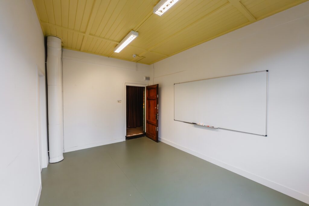 Empty classroom with a whiteboard, yellow ceiling, and an open wooden door.