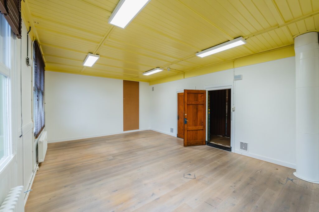 Empty room with wooden floor, yellow ceiling, white walls, and an open wooden door.