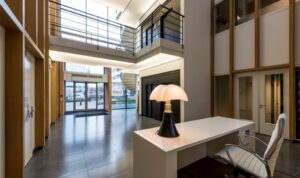 Moderne entreehal van een kantoorpand aan de Hogehilweg, met designlamp op balie en zicht op glazen voordeuren.
