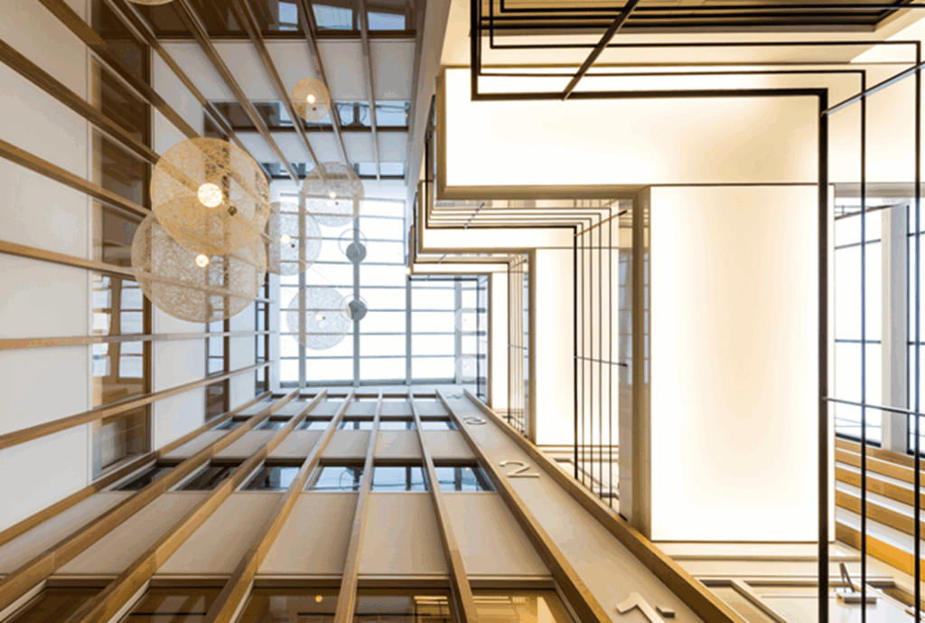 Doorkijk in het moderne atrium van Hogehilweg 17 met houten lamellen, hanglampen en strakke lijnen naar boven.