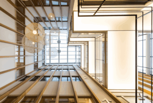 Doorkijk in het moderne atrium van Hogehilweg 17 met houten lamellen, hanglampen en strakke lijnen naar boven.