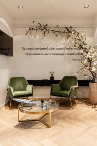 Stijlvolle wachtruimte met twee groene fauteuils, een ronde glazen salontafel en een muurquote van Johan Cruijff.