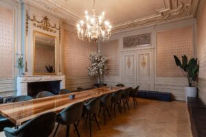 Luxe vergaderruimte aan het Rokin met een lange houten tafel, fluwelen stoelen, sierlijke wanddecoratie en kroonluchter.