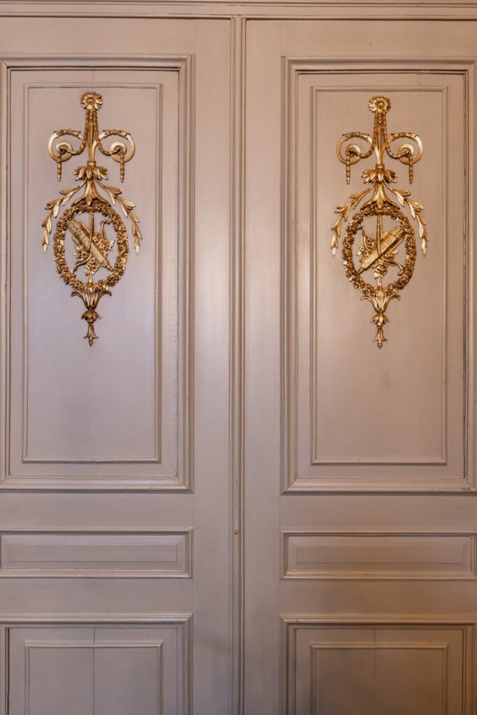 Houten paneeldeuren met gouden, symmetrische ornamentversiering in een klassiek interieur aan het Rokin.