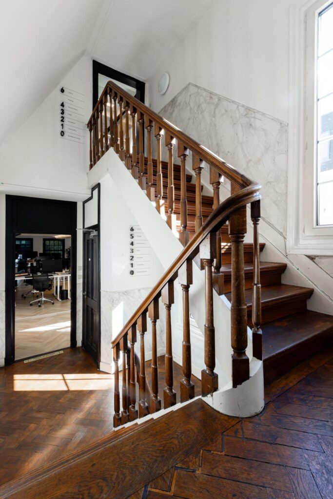 Houten trap met klassiek hekwerk in een licht trappenhuis aan het Rokin, met zicht op een modern kantoor.
