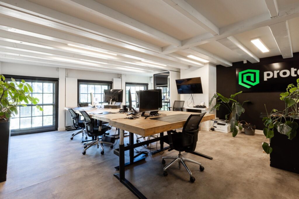 Modern kantoorinterieur op de Rokin met houten bureau, ergonomische bureaustoelen, computers en groene beplanting.