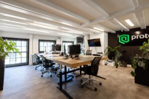 Modern kantoorinterieur op de Rokin met houten bureau, ergonomische bureaustoelen, computers en groene beplanting.