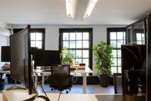 Moderne kantoorruimte aan het Rokin met bureaus, computerschermen en grote kamerplanten voor ramen met zwarte kozijnen.
