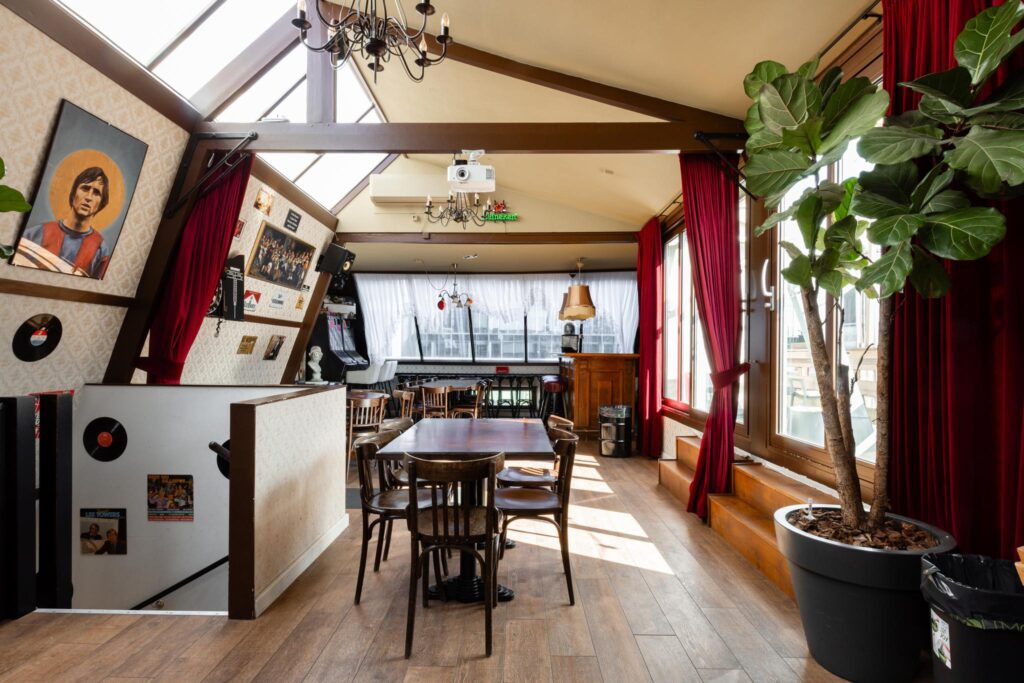 Knusse bovenverdieping van een café aan het Rokin met houten vloeren, vintage decor en grote ramen met rood fluwelen gordijnen.