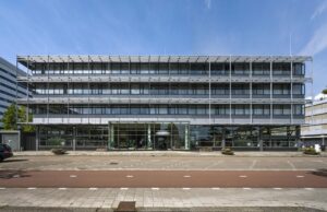 Modern kantoorgebouw aan de Kabelweg in Amsterdam met glazen entree en 'Te Huur'-borden zichtbaar.
