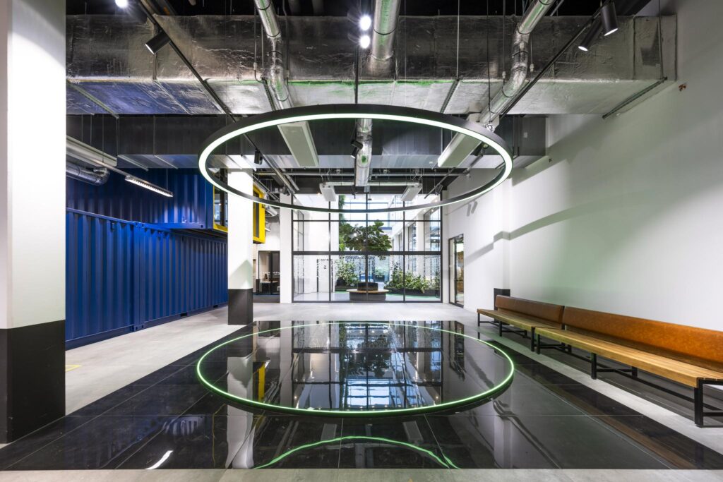 Moderne kantoorlobby aan de Kabelweg met industriële details, spiegelend zwart vloerpaneel en grote ronde LED-verlichting.