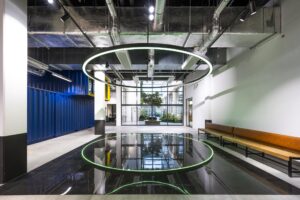 Moderne kantoorlobby aan de Kabelweg met industriële details, spiegelend zwart vloerpaneel en grote ronde LED-verlichting.