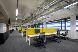 Modern kantoorpand aan de Kabelweg met open werkplekken en gele tussenschotten.
