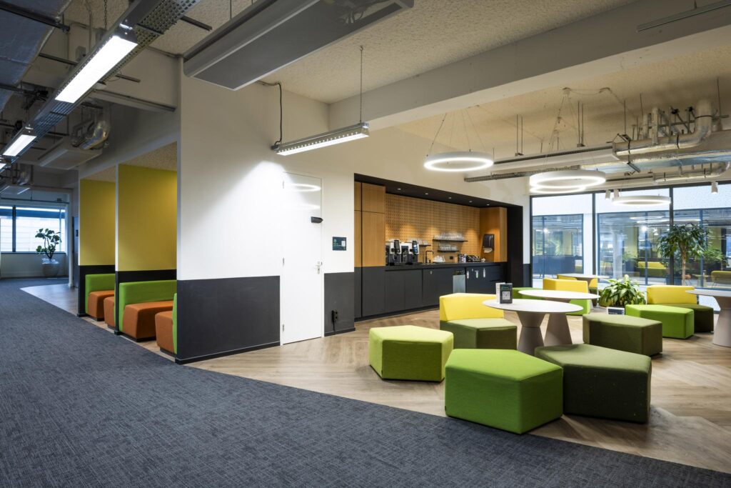 Moderne kantoorlounge aan de Kabelweg met kleurrijk meubilair, koffiecorner en veel daglicht.