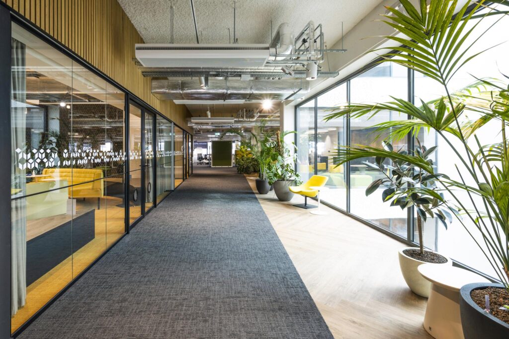 Moderne kantoorruimte aan de Kabelweg met glazen wanden, veel planten en een gele designstoel bij het raam.