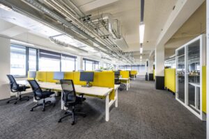 Modern en licht kantoorinterieur aan de Kabelweg met open werkplekken en gele scheidingspanelen.