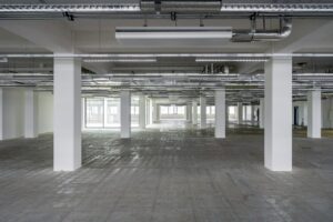 Leegstaand kantoorpand aan de Kabelweg met betonnen vloer en zichtbare plafonleiding.