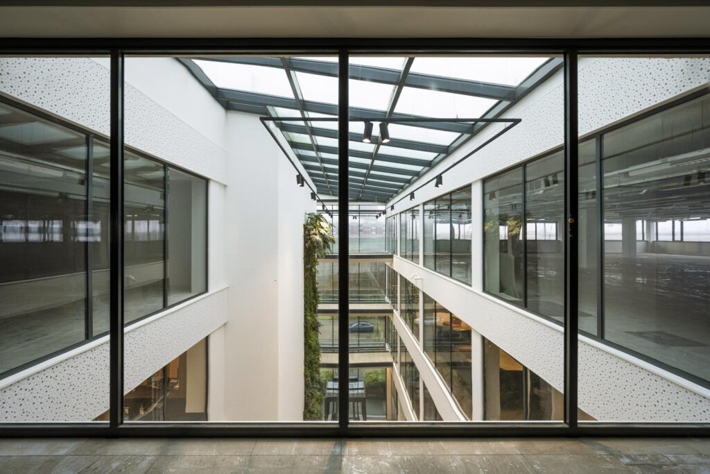 Glaswand met uitzicht op een modern atrium met meerdere etages in een kantoorgebouw aan de Kabelweg.