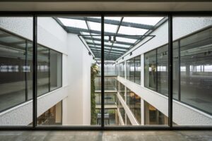 Glaswand met uitzicht op een modern atrium met meerdere etages in een kantoorgebouw aan de Kabelweg.