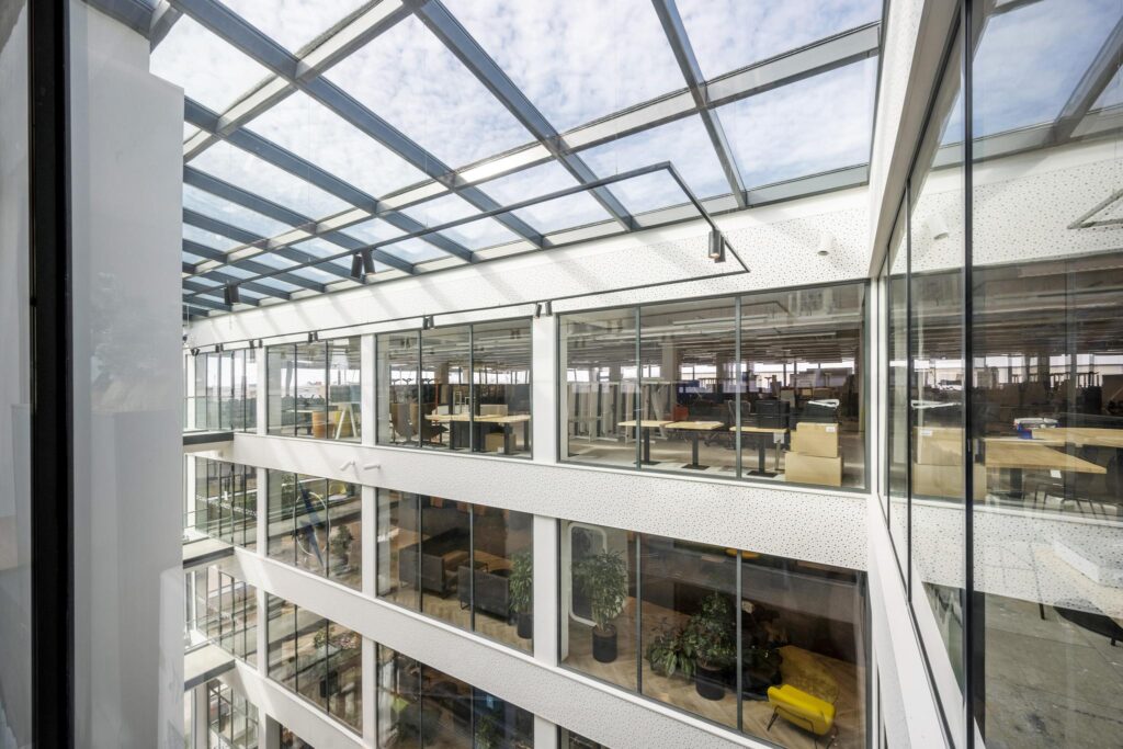 Licht atrium van kantoorpand aan de Kabelweg met meerdere verdiepingen en glazen binnengevels.