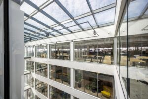 Licht atrium van kantoorpand aan de Kabelweg met meerdere verdiepingen en glazen binnengevels.