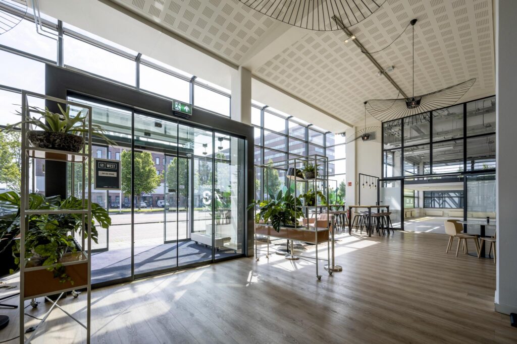 Moderne, lichte entreehal van een kantoor aan de Kabelweg met glazen gevel, planten en zithoeken.