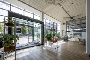 Moderne, lichte entreehal van een kantoor aan de Kabelweg met glazen gevel, planten en zithoeken.