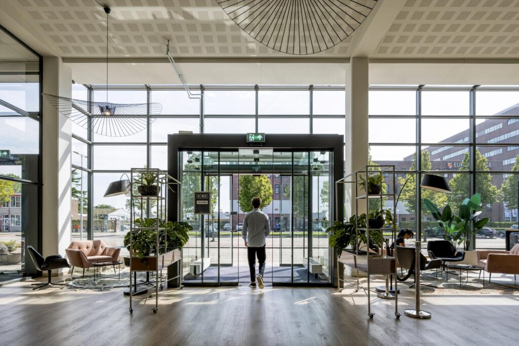 Man loopt een modern kantoorgebouw aan de Kabelweg in Amsterdam uit via een glazen draaideur.