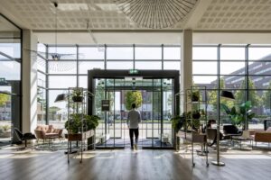 Man loopt een modern kantoorgebouw aan de Kabelweg in Amsterdam uit via een glazen draaideur.