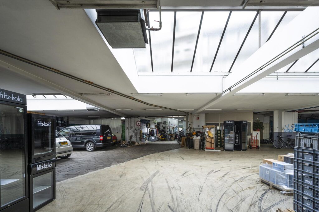 Covered industrial garage space on Baarsjesweg with parked vehicles, storage crates, and Fritz-Kola vending machines.