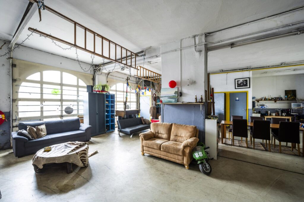 Spacious and eclectic living area with mismatched sofas, a large dining table, and industrial-style decor on Baarsjesweg.