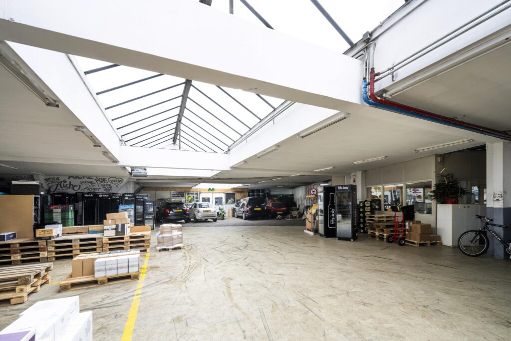 Spacious indoor warehouse with skylights, parked cars, pallets, and stacked boxes at Baarsjesweg.