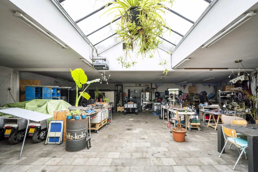 Spacious and well-lit industrial workshop on Baarsjesweg, filled with tools, workbenches, plants, and creative equipment.
